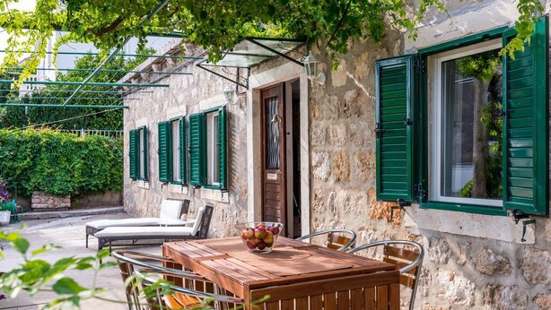 A stone building with green shutters, a wooden table with chairs, and a bowl of fruit. - near Dubrovnik City Walls (Dubrovnik)