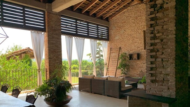Uma área de pátio coberta com parede de tijolos, espaço de estar com almofadas, mesa e cadeiras.