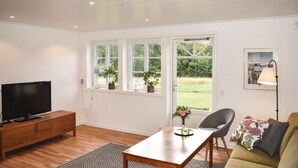 A living room with a TV on a wooden cabinet, a dining table with chairs, and a sofa. There are windows with plants on the windowsill and a picture on the wall. - Lovely home in Unnaryd with WiFi (Unnaryd)
