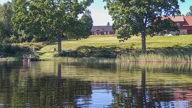 A house with a red roof and white trim, surrounded by trees and a pond. - Lovely home in Unnaryd with WiFi (Unnaryd)