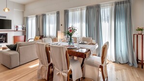 Een moderne woonkamer met een eettafel voor vier personen, een bank en een aan de muur bevestigde televisie.