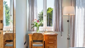 Een slaapkamer met een houten bureau, een stoel, een bed en een raam met gordijnen.