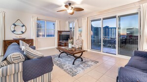 A spacious living room with a ceiling fan, a large window, and a sliding glass door leading to a balcony. - special, complete and fun (Miramar Beach)