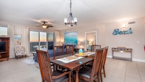 A dining area with a wooden table, chairs, and a chandelier. There is a large window with curtains, a painting of a wave, and a sign that reads "Beach" on the wall. - special, complete and fun (Miramar Beach)
