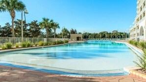 A swimming pool with a clear blue water, surrounded by palm trees and a building with a white facade. - special, complete and fun (Miramar Beach)