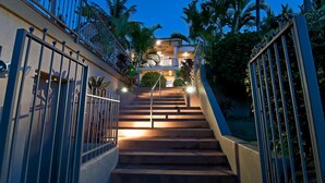 A staircase leading to a balcony with a view of palm trees, surrounded by a gated area with metal railings.