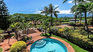 A swimming pool with a turtle, surrounded by lush greenery and palm trees, with a view of the ocean in the background.