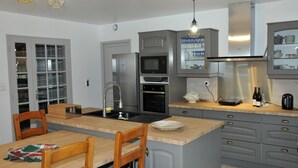 A modern kitchen with grey cabinets, a central island, stainless steel appliances, and a dining area with wooden chairs.