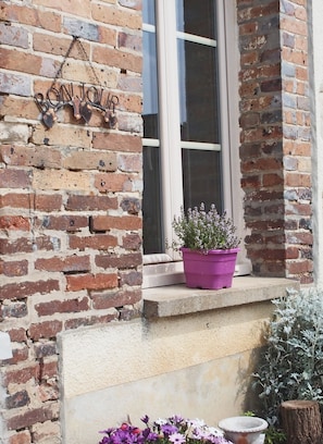 A brick wall with a 'BONJOUR' sign, a window, and a purple flower pot on a ledge. - La Ferme de Flo' (Evry)