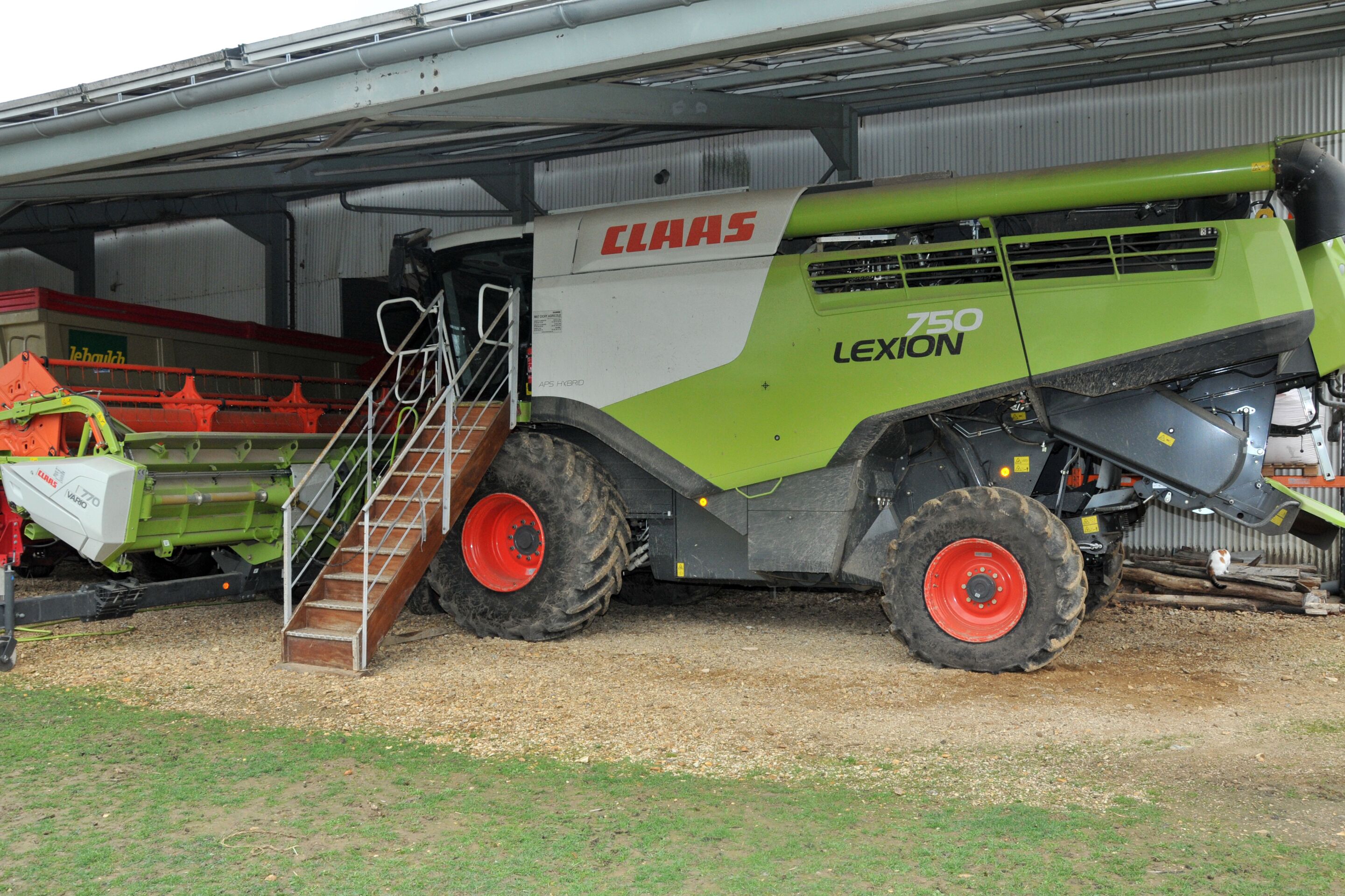 Una máquina agrícola grande, concretamente una CLAAS LEXION 750, estacionada al aire libre con una escalera metálica que lleva a su cabina.