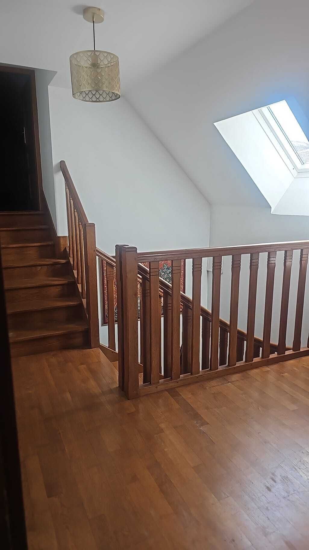 Eine Holztreppe mit Geländer, einer Hängeleuchte und einem Oberlicht.