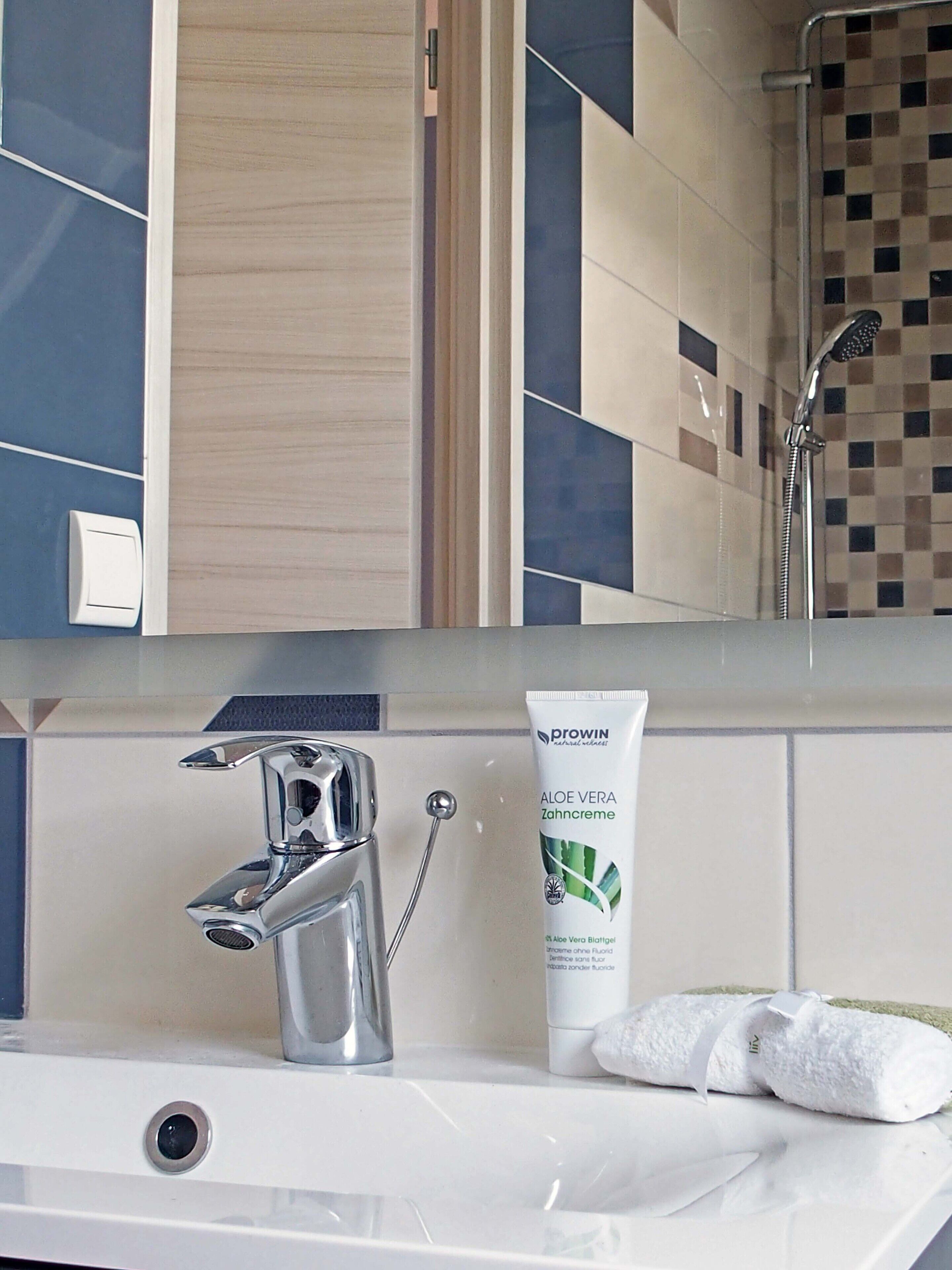 Ein Badezimmer mit einem modernen Waschbecken, einer Duschbrause und einer Tube Aloe Vera Creme.