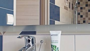 Un baño con un lavamanos moderno, un cabezal de ducha manual y un tubo de crema de aloe vera.