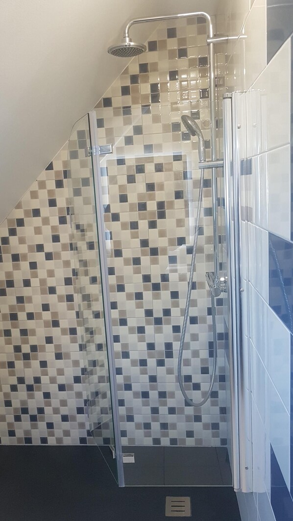 Zona de ducha con mampara de vidrio, pared con azulejos y ducha.