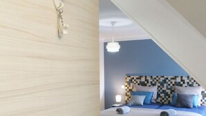 A bedroom with a checkered headboard, a bed with blue and grey pillows, and a white bedside lamp.