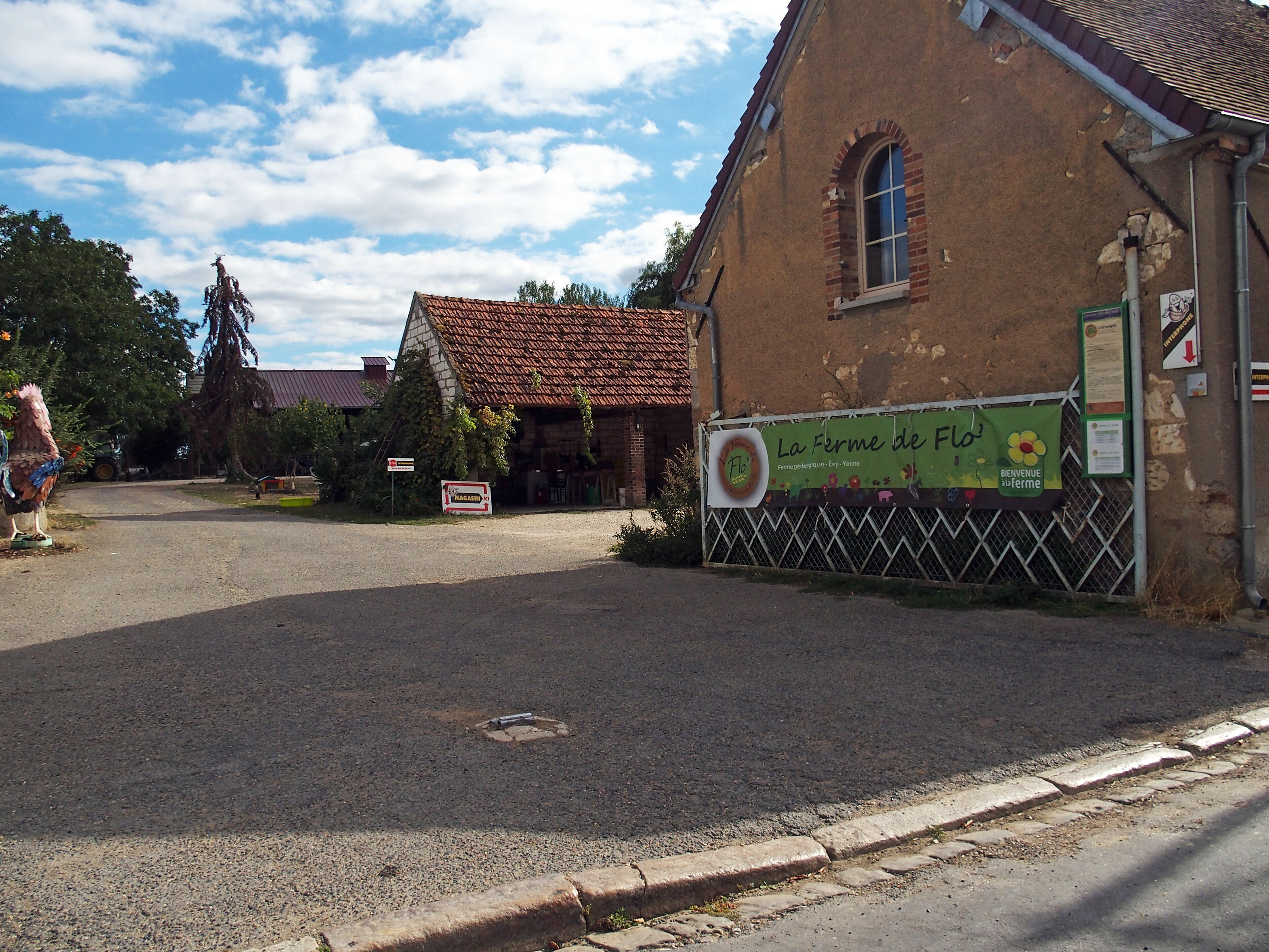 A rustic building with a tiled roof, a signboard, and a fenced area.