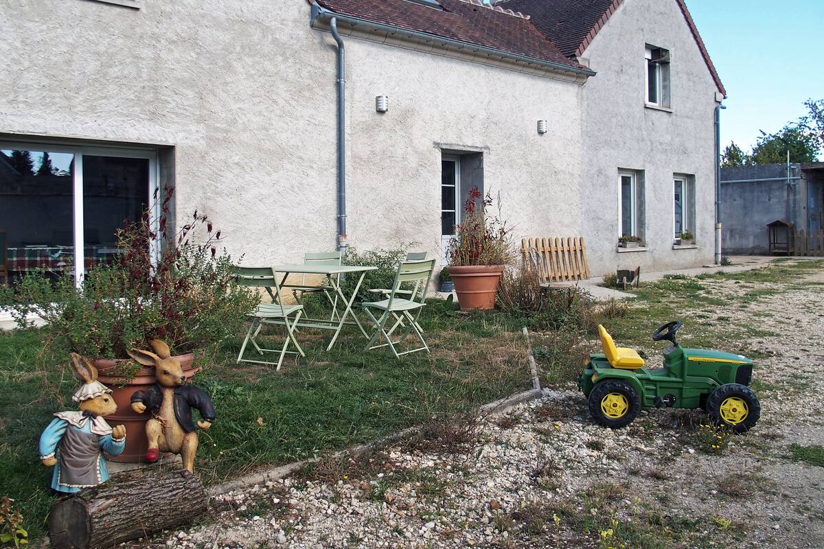Ein rustikales Haus mit einem Schotterweg, einem grünen Traktor und Gartenmöbeln.