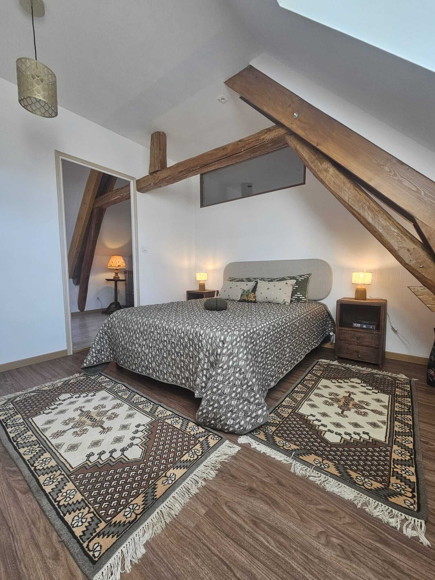 A bedroom with a sloped ceiling, a bed with patterned bedding, two bedside lamps, and a rustic wooden beam.