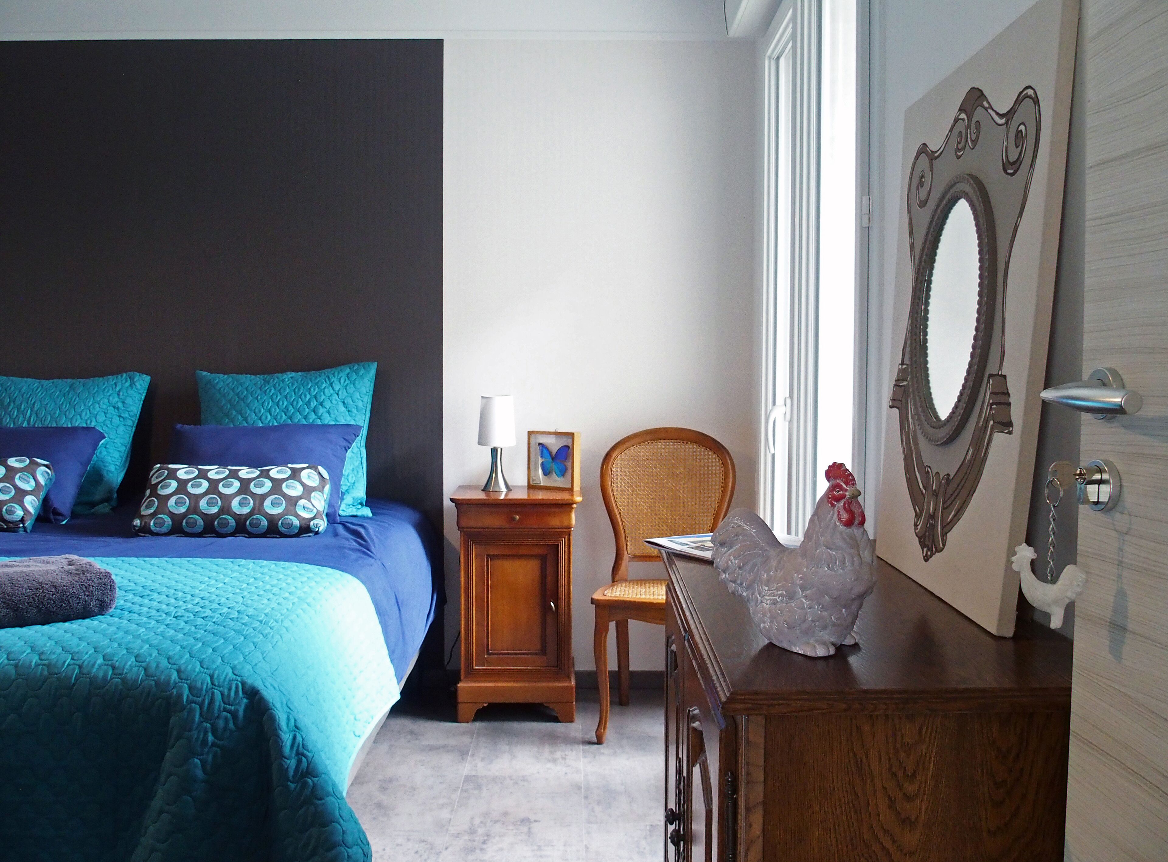 A bedroom with a bed, a nightstand, a chair, a dresser, and a mirror.