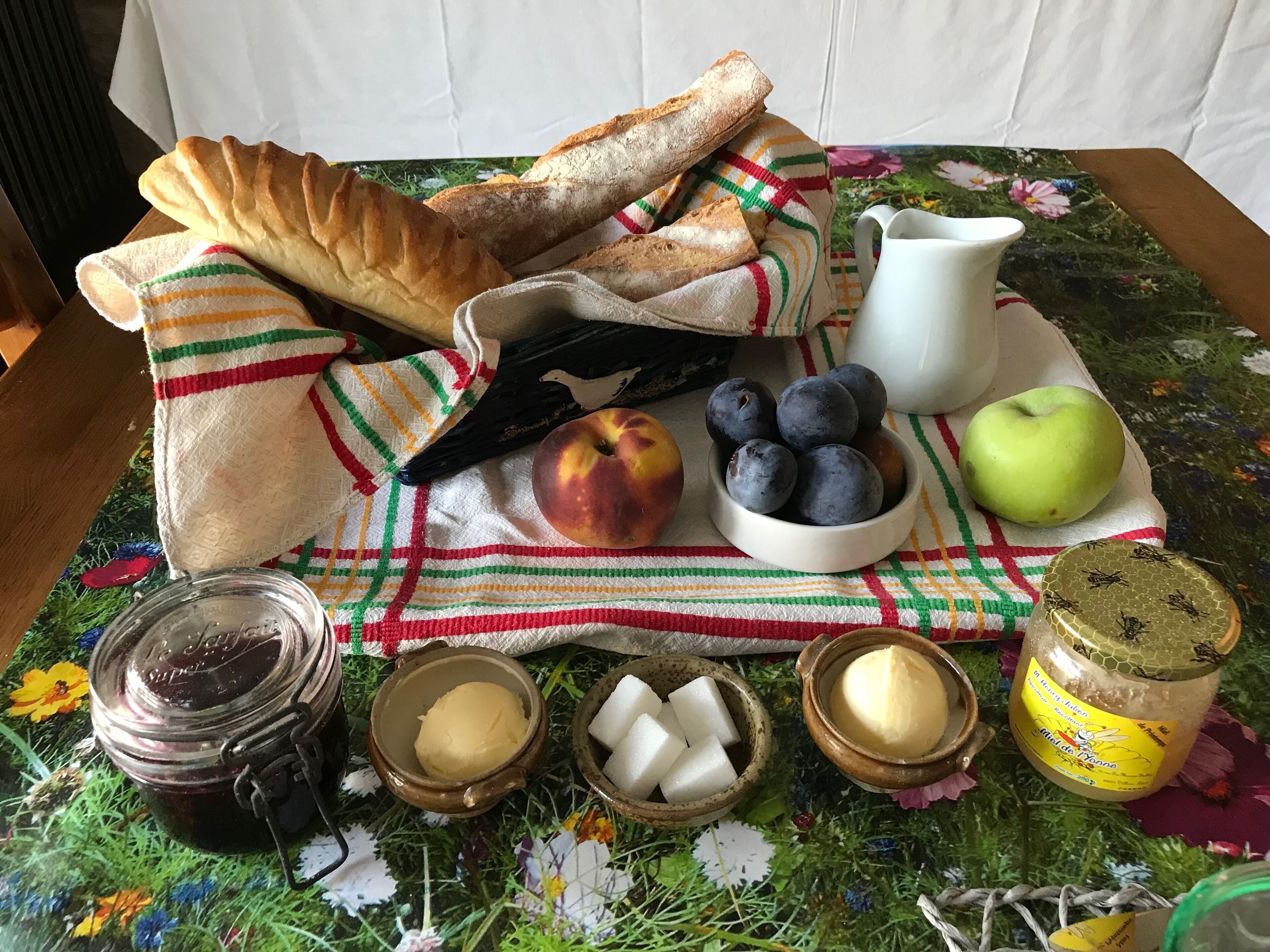Una mesa con pan, una jarrón, un tazón de arándanos, una manzana, frascos de miel y cubos de azúcar.