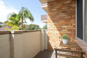 A balcony with a brick wall, a wooden table, and a potted plant.