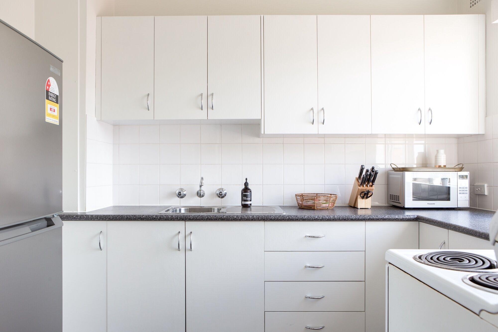 A kitchen with white cabinets, a stainless steel sink, a microwave, and a stove.