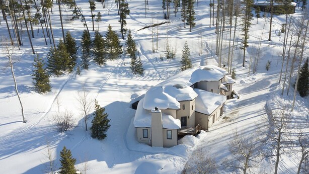 Ett snötäckt bostadsområde med ett stort hus som har en cirkelformad design och omges av träd och en klar himmel.
