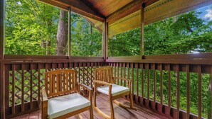Una terraza de madera con dos mecedoras y vistas a un bosque.