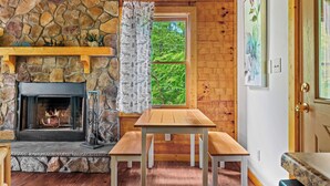 Una habitación acogedora con chimenea de piedra, una mesa de madera y ventana con vista a follaje.