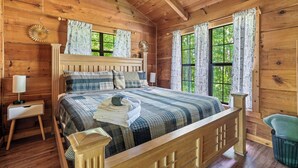 A wooden cabin bedroom with a bed, nightstand, and a window with curtains.