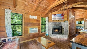 A cozy cabin interior with a stone fireplace, wooden walls, and large windows offering a view of the forest.