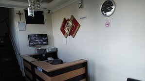 A reception desk with a clock, a TV displaying multiple channels, and a cross on the wall.