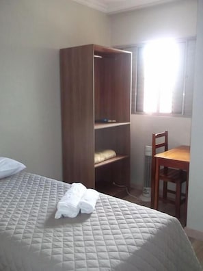Quarto com cama, guarda-roupa de madeira, cadeira e janela com luz natural.