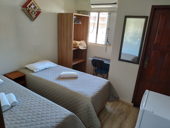 Quarto com duas camas, um guarda-roupa, uma escrivaninha e um espelho.