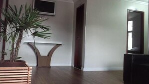 A room with a wooden floor, a potted plant, a TV mounted on the wall, and a door leading to another room.