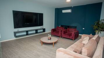 A modern living room with a flat-screen TV mounted on the wall, a red sofa, a pink sofa, and a round coffee table.