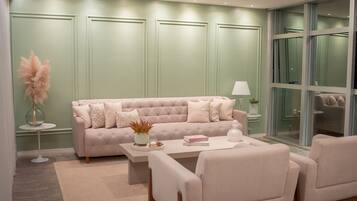 A modern living room with a beige sofa, a coffee table, and two armchairs. There is a vase with dried flowers on a side table, and a lamp on another table.
