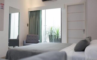 Una habitación de hotel con cama, una silla, un escritorio y un amplio ventanal con cortinas.