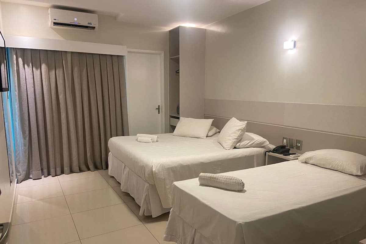 A hotel room with two beds, a bedside table with a phone, and a curtain.