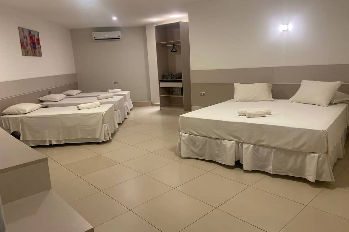 A hotel room with four single beds and one double bed, all neatly made with white linens.