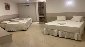 Une chambre d’hôtel avec quatre lits simples et un lit double, tous parfaitement préparés avec du linge de lit blanc.