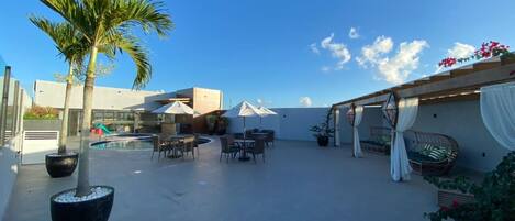 A rooftop patio with outdoor seating, a palm tree, and a pool in the background.