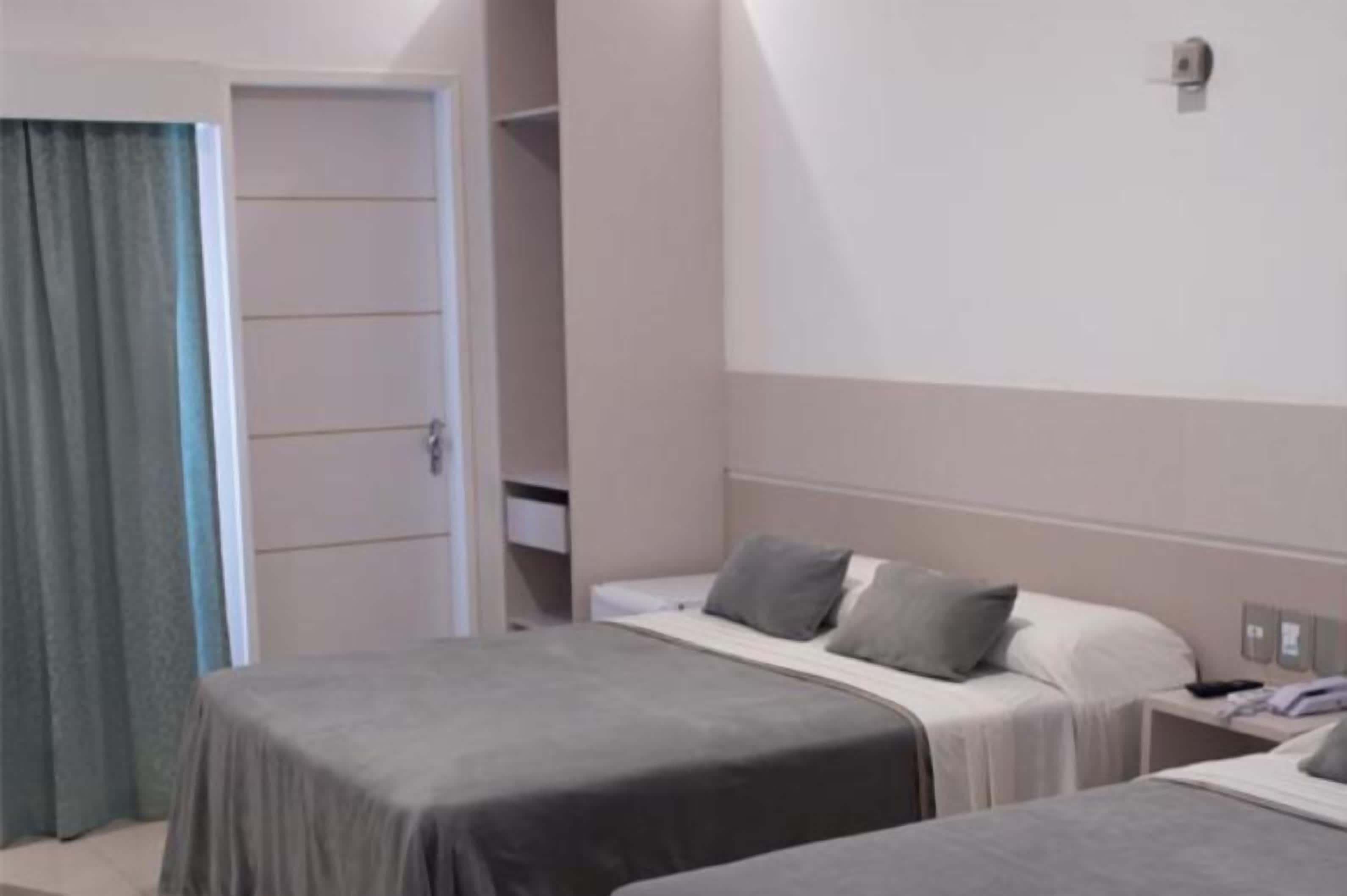 A hotel room with two beds, a wardrobe, and a small table with a lamp.