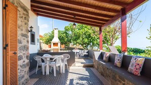An outdoor patio with stone walls, a wooden door, white plastic chairs, a table, and a stone bench with colorful cushions. - Raivinha Mother House, A traditional home in the heart of Arco da Calheta (Arco da Calheta, Madeira)