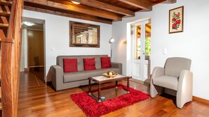 A living room with a wooden ceiling, a grey sofa with red cushions, a wooden coffee table, and a red rug. - Raivinha Mother House, A traditional home in the heart of Arco da Calheta (Arco da Calheta, Madeira)