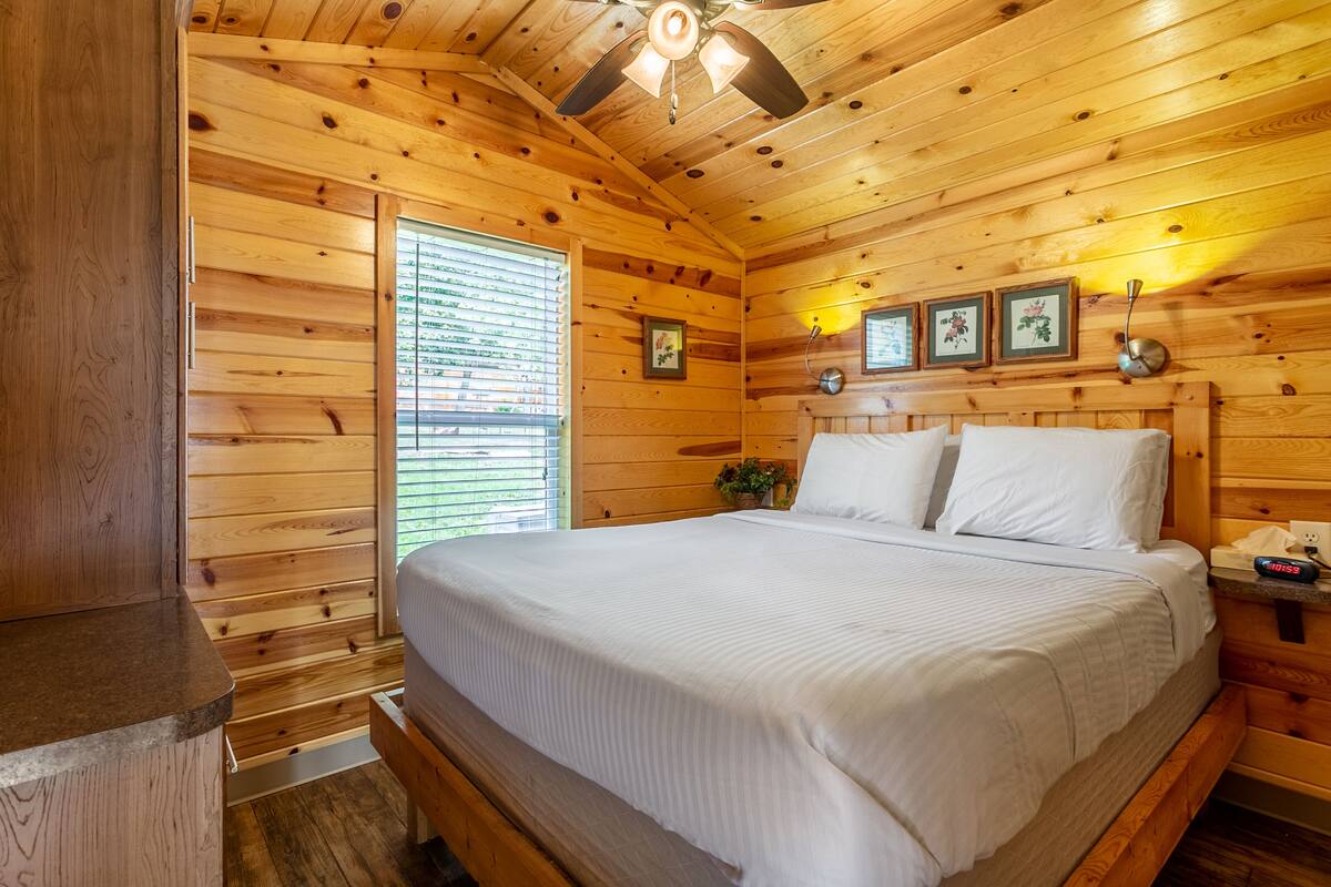 Un dormitorio de cabaña de madera con cama, mesita de noche, reloj de pared y fotografías enmarcadas.
