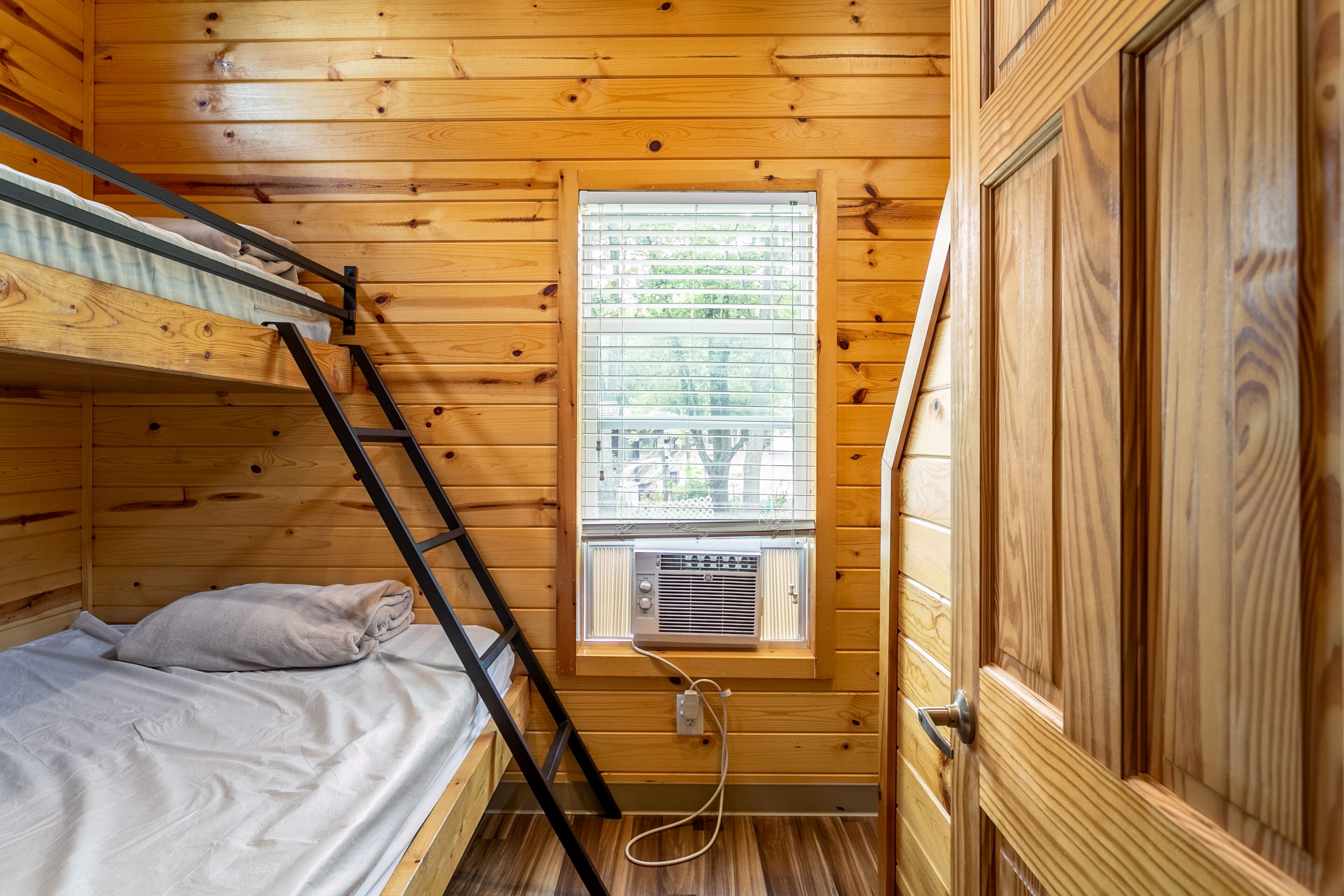 Una cabaña de madera con una cama litera, una ventana con persianas y una puerta.