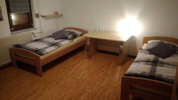 Ein kleines, schlichtes Zimmer mit zwei Holzbett, einem Schreibtisch und einer Heizung.