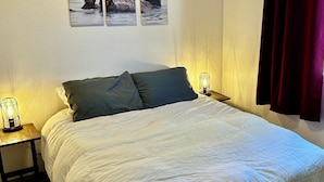 Ein Schlafzimmer mit einem Bett, zwei Nachttischen mit Lampen, einem Wandbild von Ottern und einem roten Vorhang.