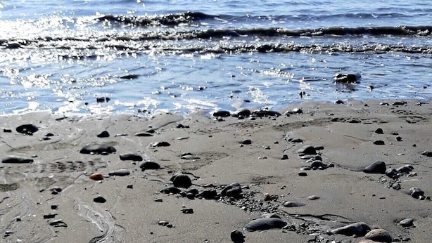 Ein Strand mit vereinzelten Felsen und Kieselsteinen.